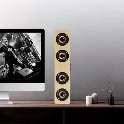 Bluetooth Speaker With Built In Mic For Everyday Home Use placed on desk beside monitor, showing four drivers