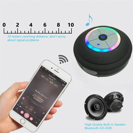 Compact Waterproof Shower And Beach Speaker With Suction Cup in black with LED ring next to smartphone showing Bluetooth music