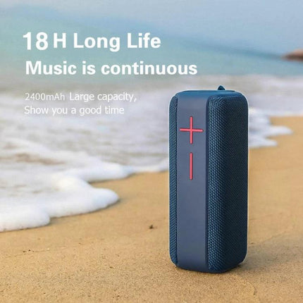 Portable Bluetooth Speaker With Carabiner For Outdoor Use clipped to a backpack on a sandy beach showing 18H playtime