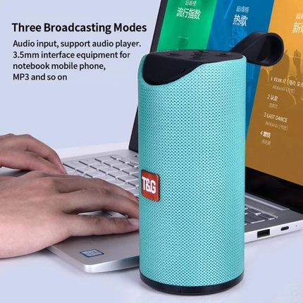 Portable Bluetooth Travel Speaker With FM Radio For Outdoor shown teal cylinder speaker next to laptop and hands typing