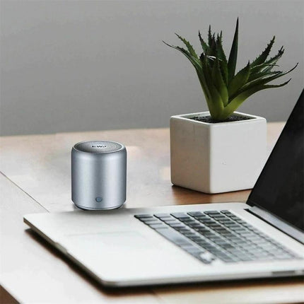 EWA Compact Portable Speaker For Home And Travel Use on desk next to laptop and plant, compact cylindrical Bluetooth speaker