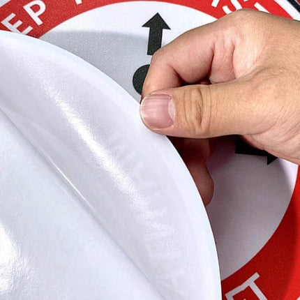 Self-Adhesive Social Distance Floor Sticker 24x24 cm being peeled and applied to an indoor floor to mark pedestrian spacing