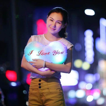 Heart Shaped English Letter Pattern Glowing Plush Pillow held by smiling person at night with soft multicolor glow