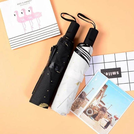 Feather Pattern Three-Folding Umbrella for Rain and Sun Protection compact black and white umbrellas with wrist straps on peach background