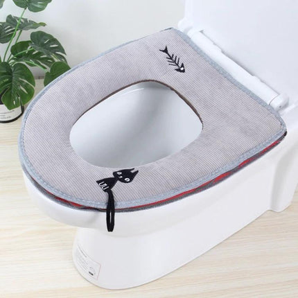 Cozy Washable Toilet Seat Cover for Cold Days — soft grey washable cushion with cat and fishbone embroidery on a white toilet