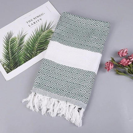 Striped Cotton Bath Towel With Tassels For Everyday Use folded green geometric towel with white band and tassels styled with magazine and flowers