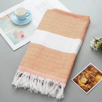 Striped Cotton Bath Towel With Tassels For Everyday Use folded peach patterned towel with white stripe and tassels on tabletop