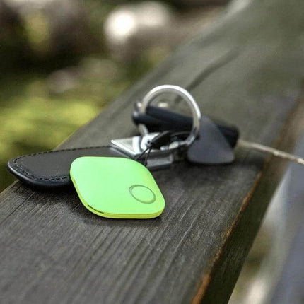 Smart Bluetooth Anti-Lost Device for Keys and Wallets attached to keyring on a bench, compact green Bluetooth tracker