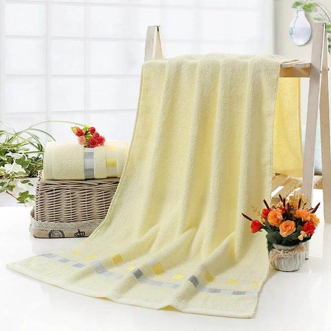 Cotton Plain Bath Towel 140x70 For Daily Bathroom Use - soft yellow cotton towel draped over rack with matching rolled towel and flowers