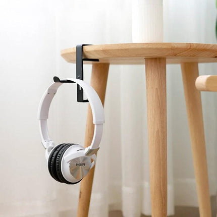 Under Desk Metal Headphone Hook For Desk Organization And Storage hanging white headphones on a black clamp under a wooden table