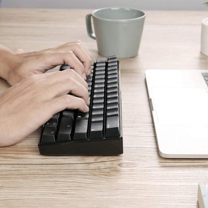 Wireless 61-Key Mechanical Keyboard for Gaming and Office Use on desk next to laptop, compact ABS build with hands typing, USB and Bluetooth modes