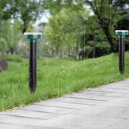 Solar Mouse Repeller Round Design For Patios And Gardens installed along a rainy garden path, solar panel top and stake in grass