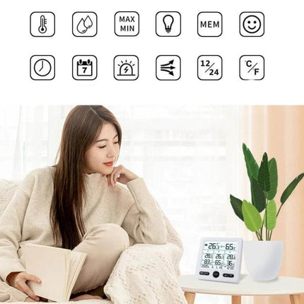 Wireless Thermometer And Hygrometer With Color Alarm on a table showing indoor readings next to a woman reading in a cozy room