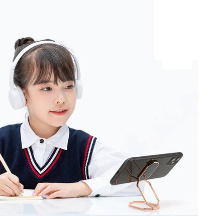 Magnetic Zinc Alloy Phone Ring Holder for Cars and Daily Use shown propping a phone on a desk while a student studies with headphones