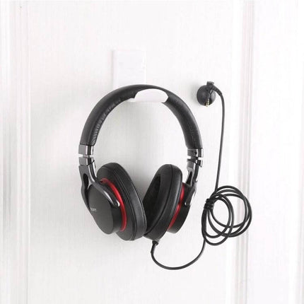 Adhesive Headphone Hanger Bracket For Wall Or Desk Storage holding black over-ear headphones on white wall