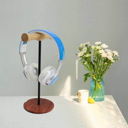 Beech Wood Headphone Stand With Metal Base For Desk holding headphones on a desk beside flowers and mug