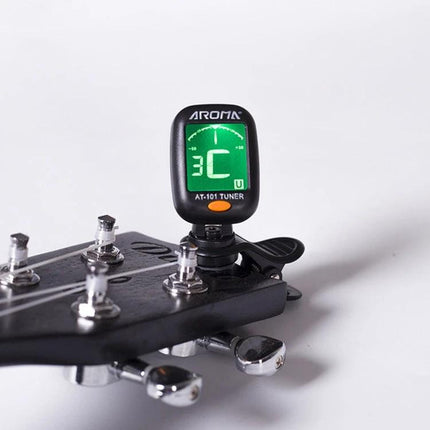 Aroma Clip-On Tuner for Everyday Instrument Tuning at Home clipped to a guitar headstock showing green digital display