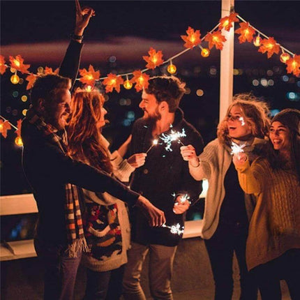 Maple Pumpkin Lantern String Lights For Halloween Decor draped above friends holding sparklers on a cozy outdoor balcony