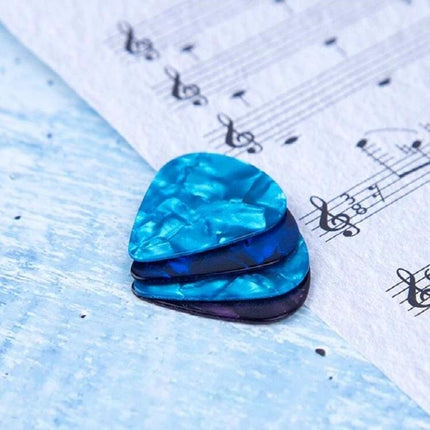Guitar Picks for Everyday Music Practice at Home — three blue pearloid picks on sheet music for at-home guitar practice