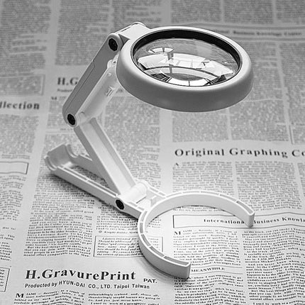 Handheld LED Magnifier for Everyday Reading and Close Inspection showing foldable acrylic lens and ABS frame on newspaper