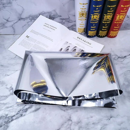 Wrinkled Reflective Tin Foil Paper for Photography Backgrounds folded on marble surface with open book and decorative books