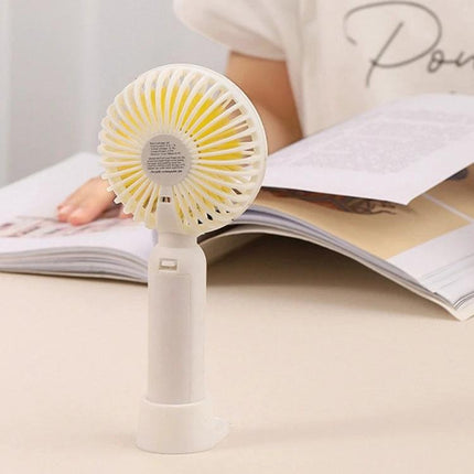 Portable Handheld Mini Fan for Outdoor and Indoor Cooling compact white handheld fan on desk beside open book, adjustable airflow