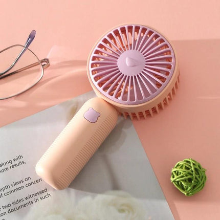 Compact Portable Handheld Electric Fan for Everyday Cooling — pastel pink handheld fan on desk with glasses and magazine