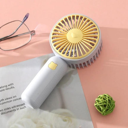 Compact Portable Handheld Electric Fan for Everyday Cooling small yellow-and-white handheld fan on desk with glasses and magazine