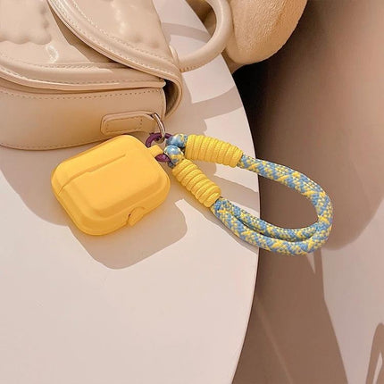 Protect Your AirPods During Daily Activities With Silicone Cover showing yellow silicone AirPods case with braided wrist strap attached to beige bag