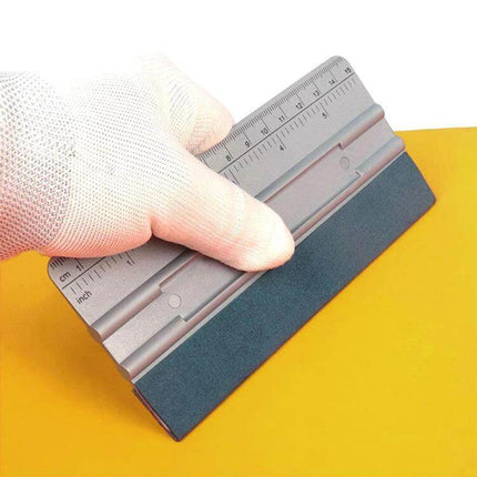 Auto Film and Wallpaper Scraper Tool with Graduated Scale held by gloved hand showing inch and cm measurements and breathable felt edge for damage-free scraping