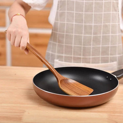 Teak Wood Kitchen Utensil Set Nonstick Pot Shovel And Spoons being used to stir a nonstick frying pan with smooth polished teak spatula