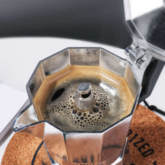 RAINBEAN 3-Cup Stovetop Moka Pot brewing rich espresso on cork coaster.