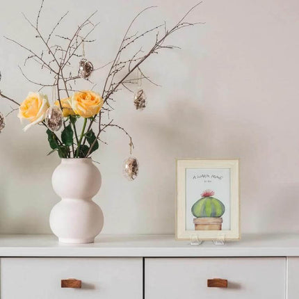 Acrylic Picture Frame Stand For Photos, Everyday Desk Display showing a clear acrylic stand holding a small framed print on a white dresser with vase of flowers