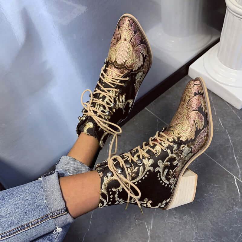 Embroidered satin ankle boots with high chunky heels in black with gold patterns worn with blue jeans.