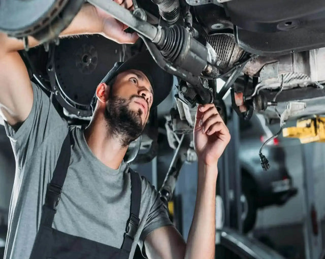 Mechanic inspecting and repairing a vehicle's undercarriage and CV axle in a garage, auto repair maintenance service
