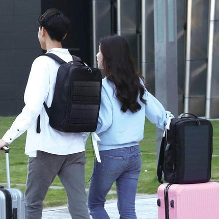 Solar Panel Backpack For Laptop With USB Charging Port worn by commuter carrying suitcase, front solar panel and USB charging port visible