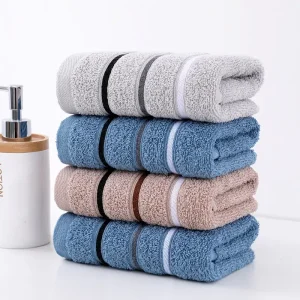 Four rolled towels in gray, blue, and beige stacked neatly with a soap dispenser in the background.