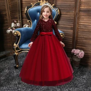 A young girl wearing a red sequin dress with a bow, seated on a blue chair.