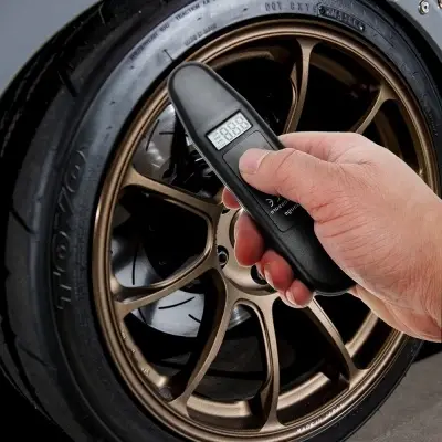 Digital Tire Pressure Gauge with Easy-to-Read Display 5 Hand Holding A Digital Tire Pressure Gauge Next To A Bronze Alloy Wheel With A Tire.