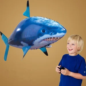 A child holding a remote control next to a large inflatable shark in a playful setting.