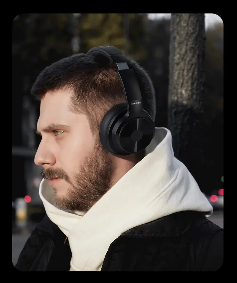 Oneodio Wireless Bluetooth Headset with ANC - Crystal-clear Sound, 70hr Battery 4 Man Wearing Black Headphones And A White Scarf, Standing Outdoors With A Neutral Expression.