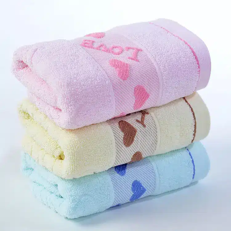 Caring Pure Cotton Face Towel for Gentle Daily Use 2 Three Stacked Towels In Pink, Yellow, And Blue With Heart Patterns On The Bands.