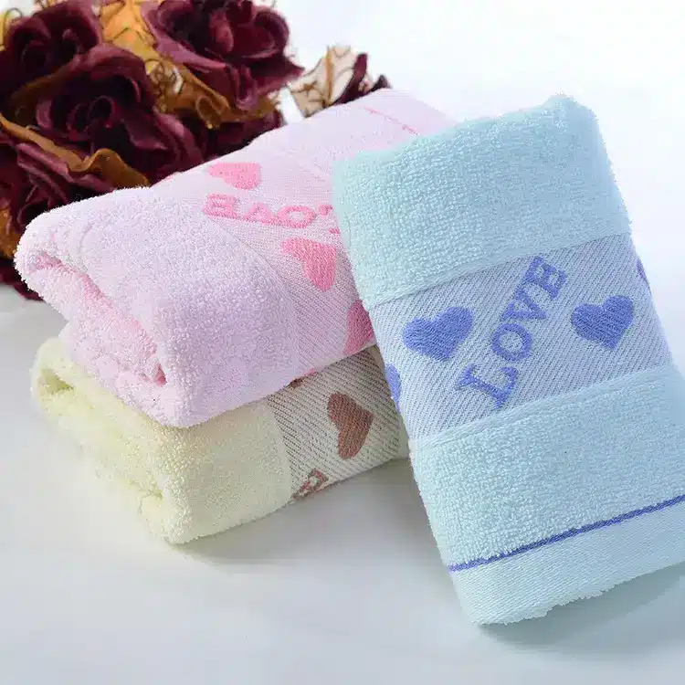 Caring Pure Cotton Face Towel for Gentle Daily Use 3 Three Soft Towels In Pink, Yellow, And Blue With Heart Patterns And The Word 'Love'.