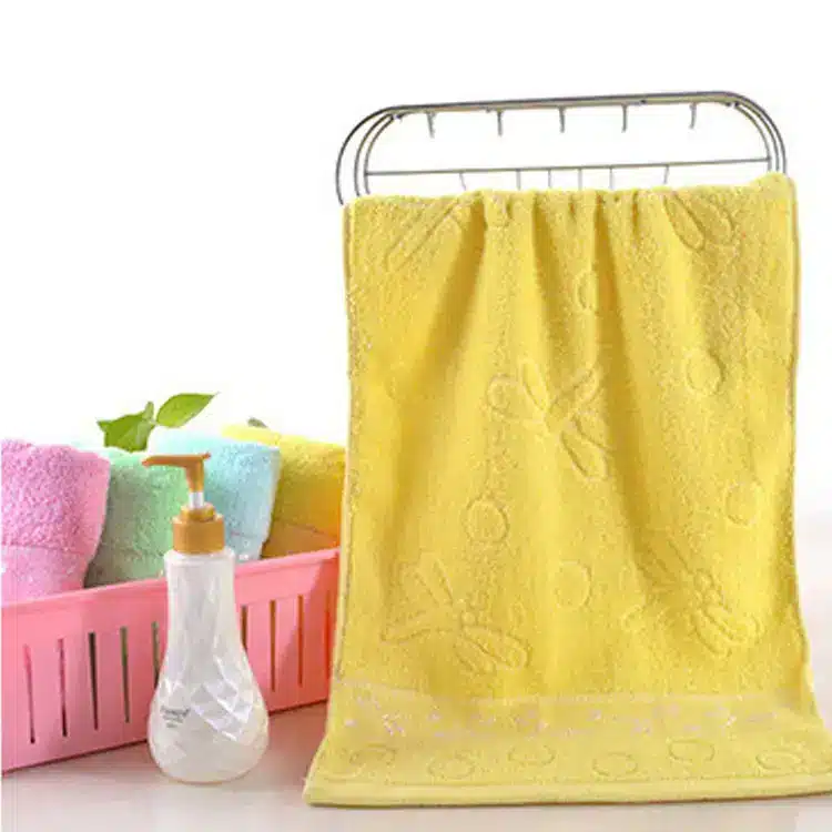 Caring Pure Cotton Face Towel for Gentle Daily Use 5 Yellow Towel With Embossed Floral Pattern Hanging On A Drying Rack Next To A Basket Of Colorful Towels.