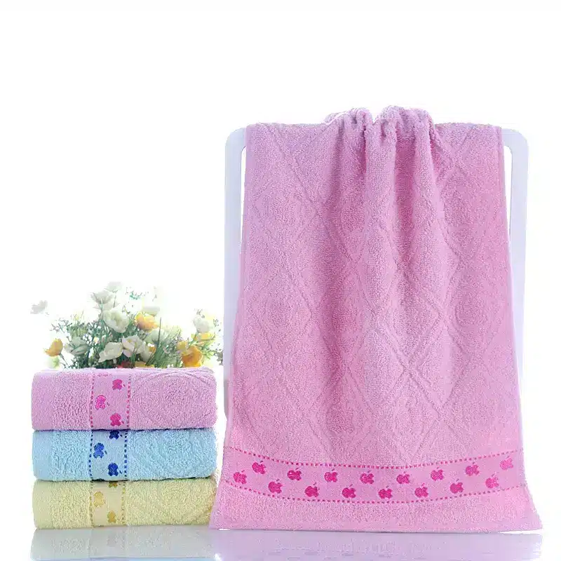 Ultra-Soft Cotton Face Towel for Daily Comfort and Care 7 A Set Of Colorful Towels In Pink, Blue, And Yellow With Decorative Patterns Displayed On A Rack.
