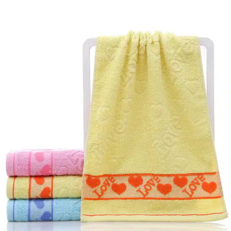 Ultra-Soft Cotton Face Towel for Daily Comfort and Care 5 Four Colorful Towels Stacked With A Yellow Towel Hanging, Featuring A Heart Pattern And 'Love' Text.