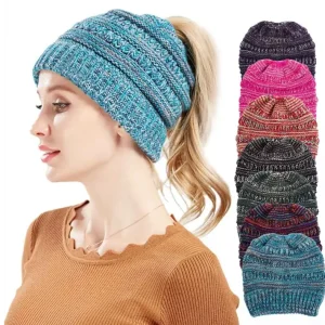 A woman wearing a blue knitted beanie hat with a ponytail, surrounded by other colored beanie hats.