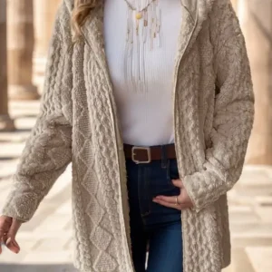 Woman wearing a beige textured jacket over a white top and blue jeans, standing outdoors.