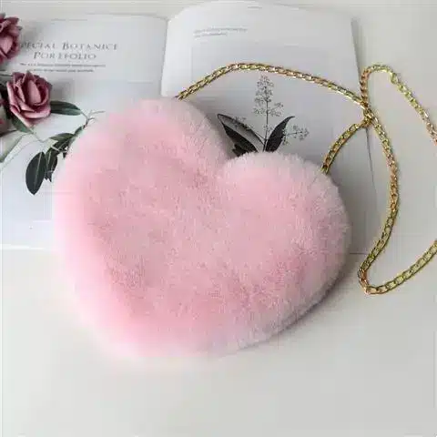 Chic Plush Chain Shoulder Bag for Valentine's Day Delight 7 Pink Heart-Shaped Plush Bag With A Gold Chain Strap Resting On A Book.