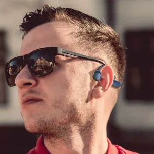Man wearing sunglasses and wireless earbuds, with a short hairstyle and a serious expression.